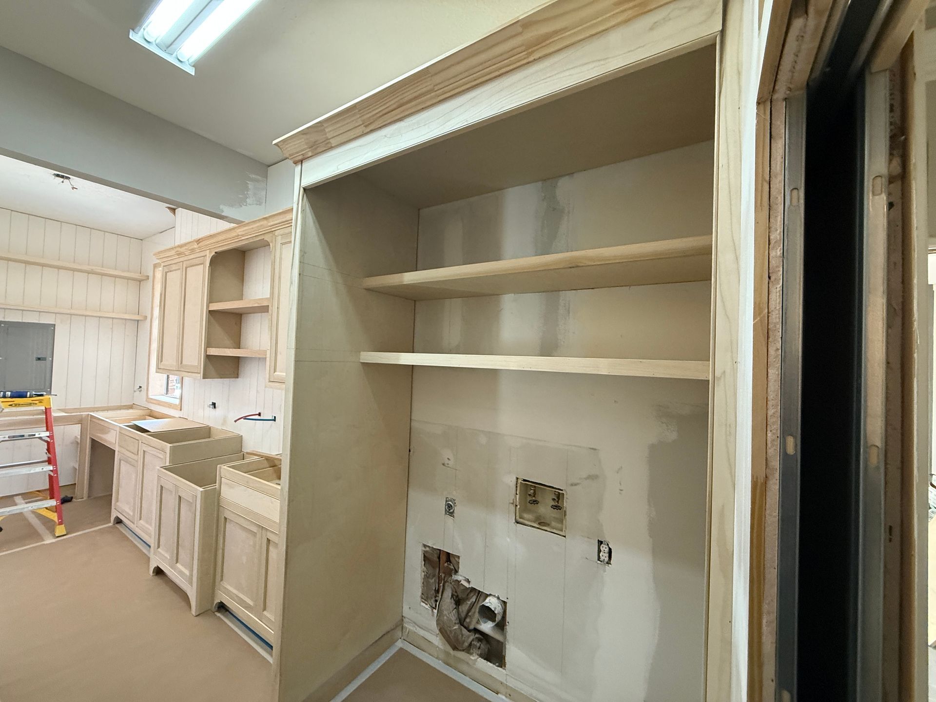 Unfinished kitchen renovation featuring wooden cabinetry, open shelving, and exposed wall cutouts for plumbing and electrical.