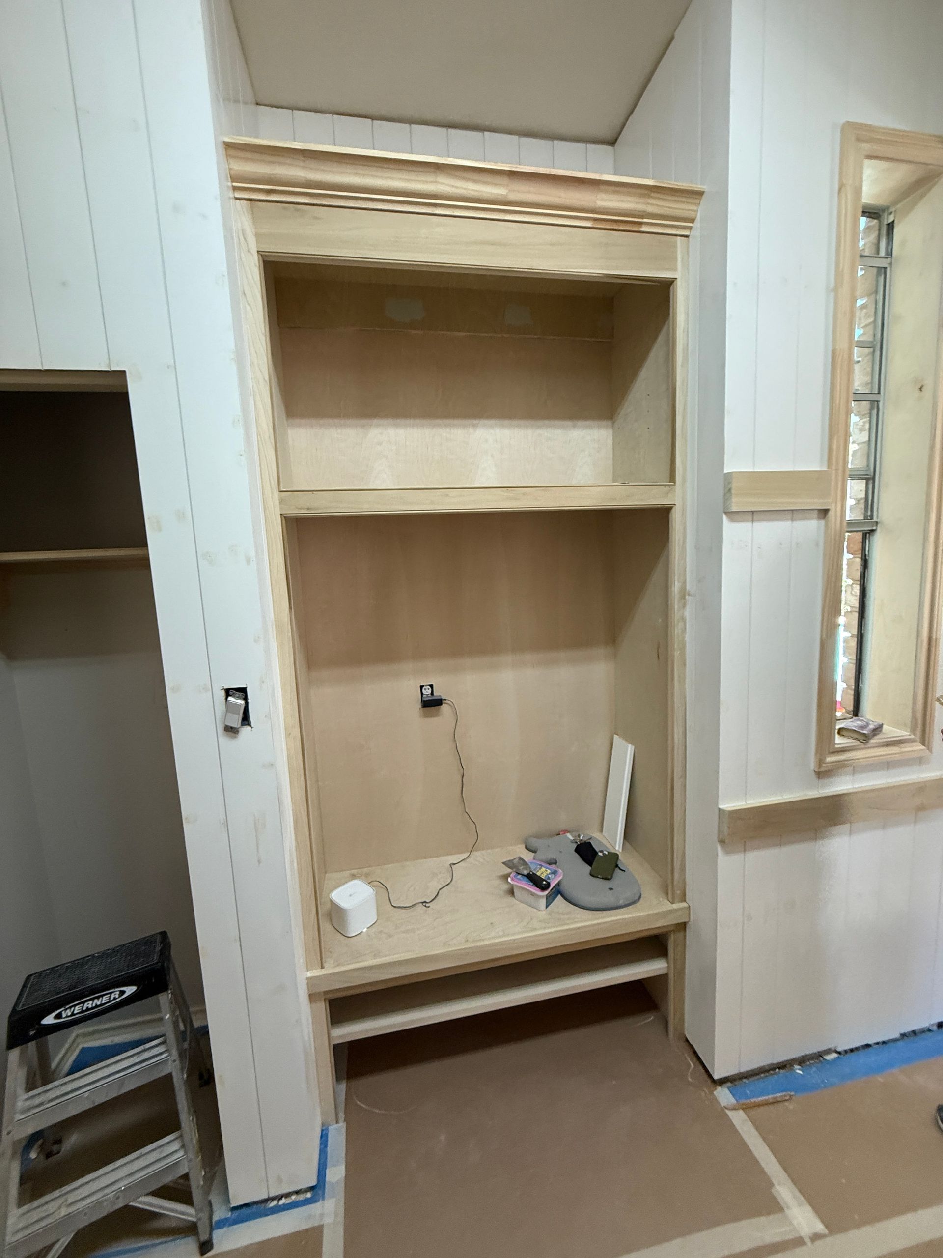 Unfinished wooden built-in shelving unit with a scalloped trim piece, centered in a room under construction.