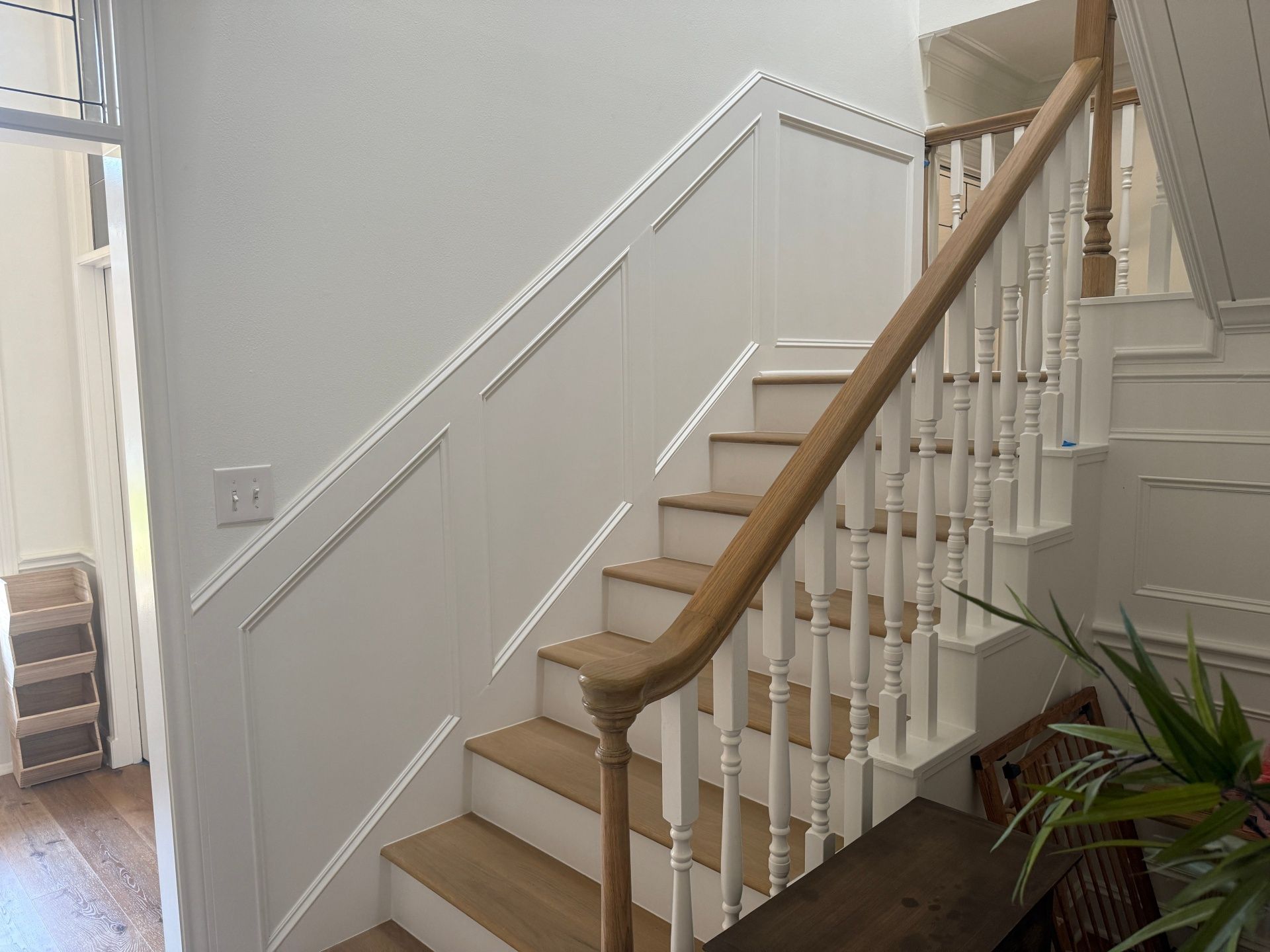 Staircase with light wood treads, white railings, and matching wall paneling in a bright indoor hallway.