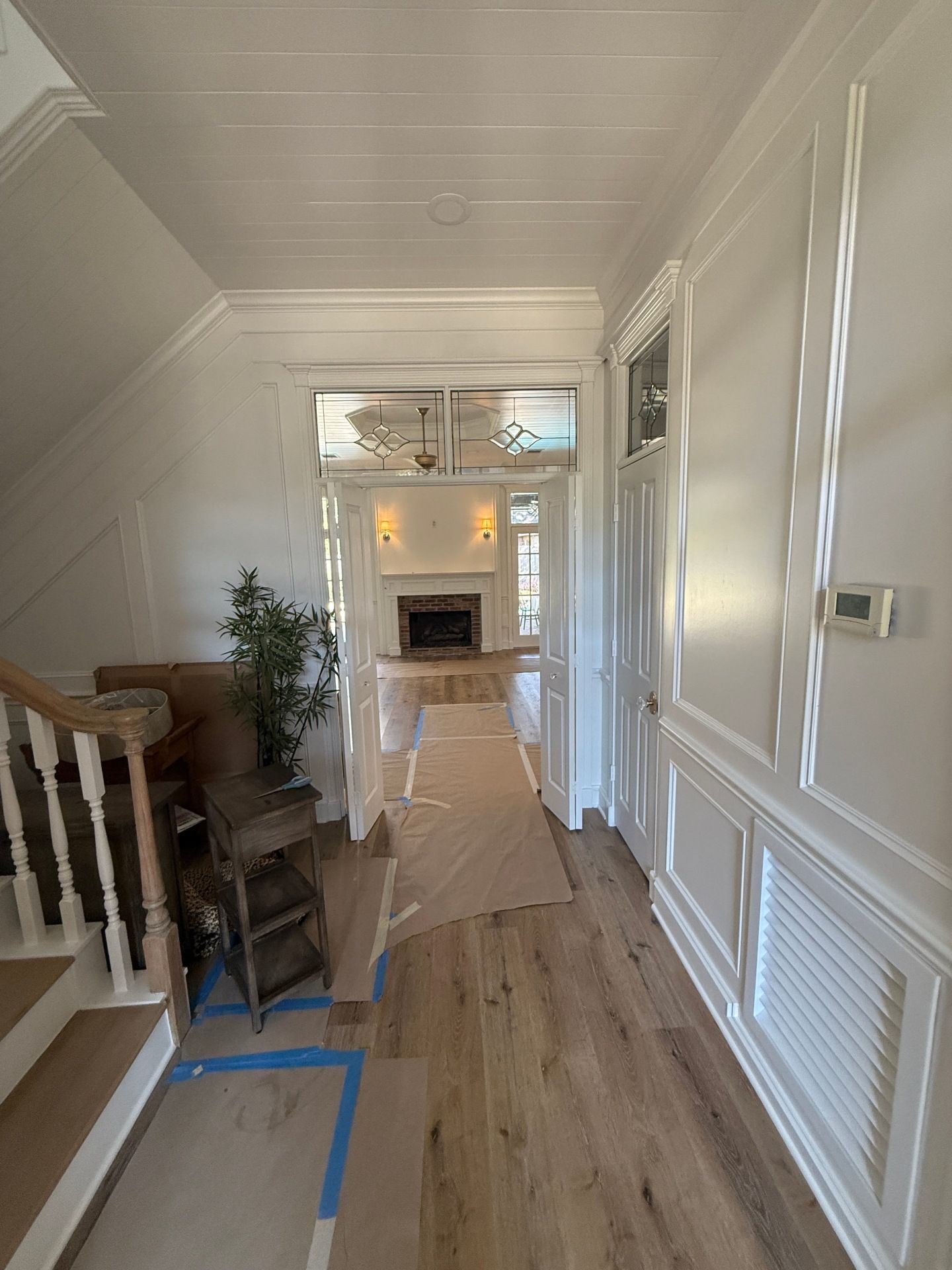 A light-filled hallway with white paneled walls and wood floors, leading through open doors toward a fireplace.