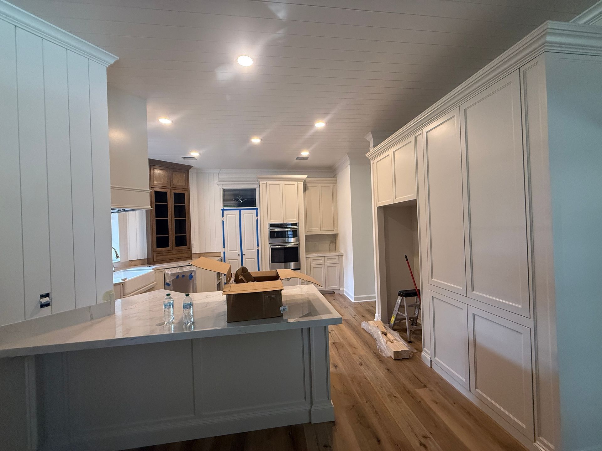 A kitchen under construction with a marble-topped island, white cabinetry, wood floors, and a step stool in the doorway.