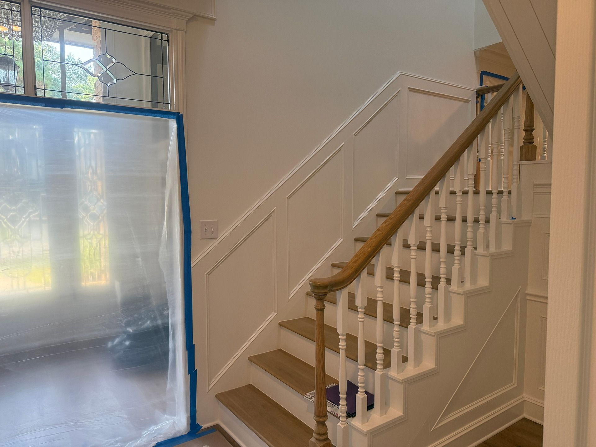 A wooden staircase with white spindles and paneling, next to a doorway covered with protective plastic sheeting.