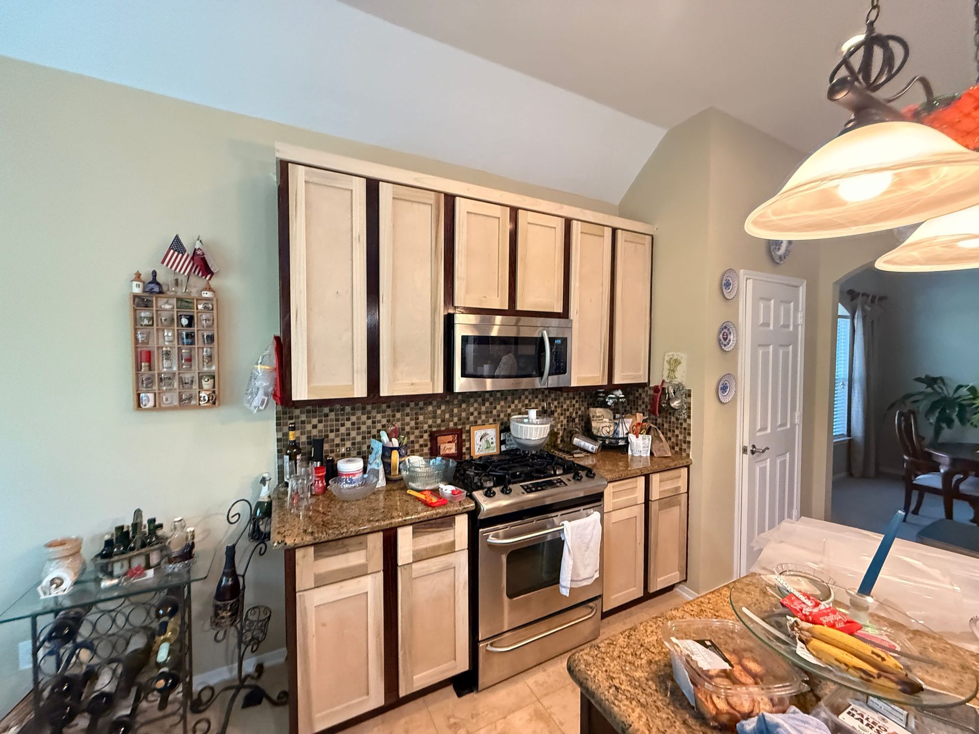 A kitchen features light wood cabinets with dark trim, stainless steel appliances, and brown granite countertops.