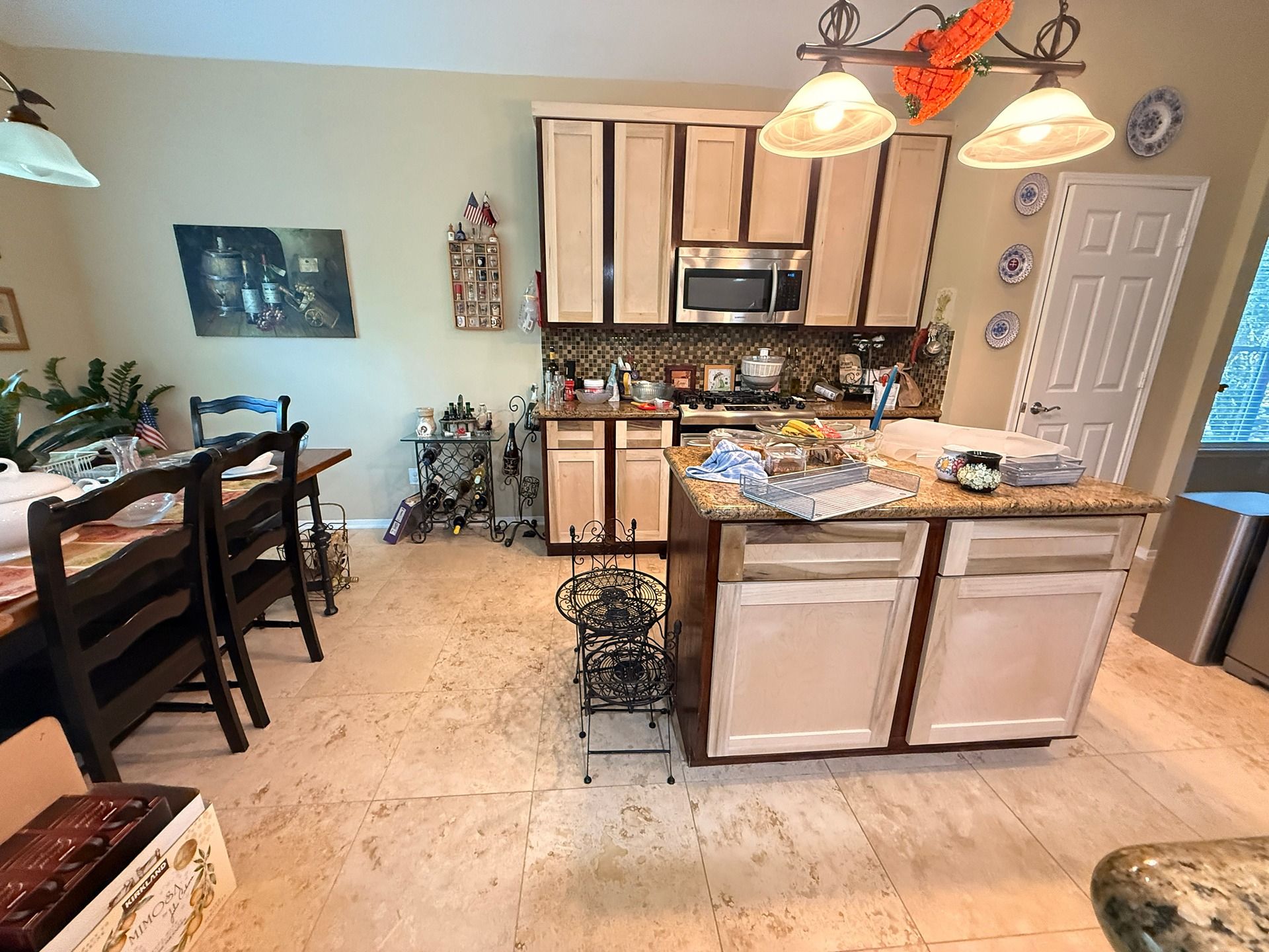 A kitchen with light wood cabinets, an island, a dining table with chairs, and tiled flooring.