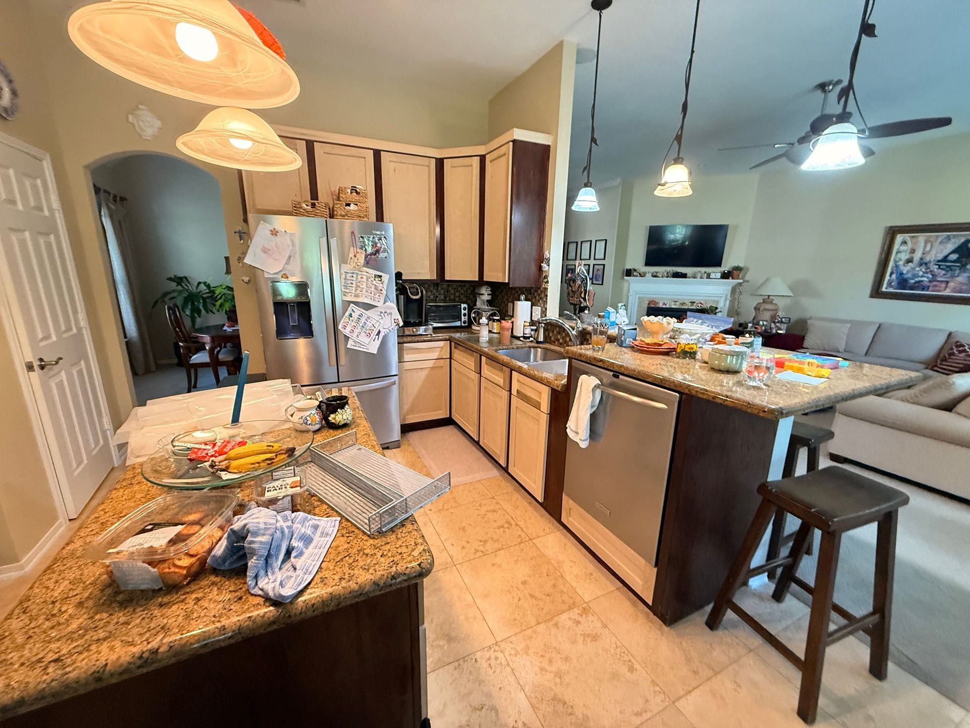 A kitchen featuring brown cabinets, granite countertops, stainless steel appliances, and an island with a wooden stool.
