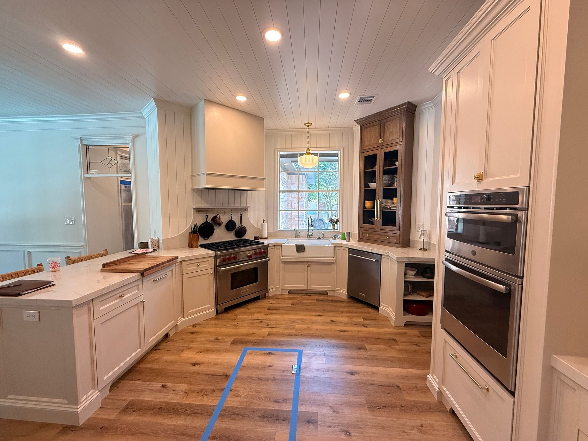 A bright kitchen featuring white cabinets, stainless steel appliances, a farmhouse sink, and light wood flooring.