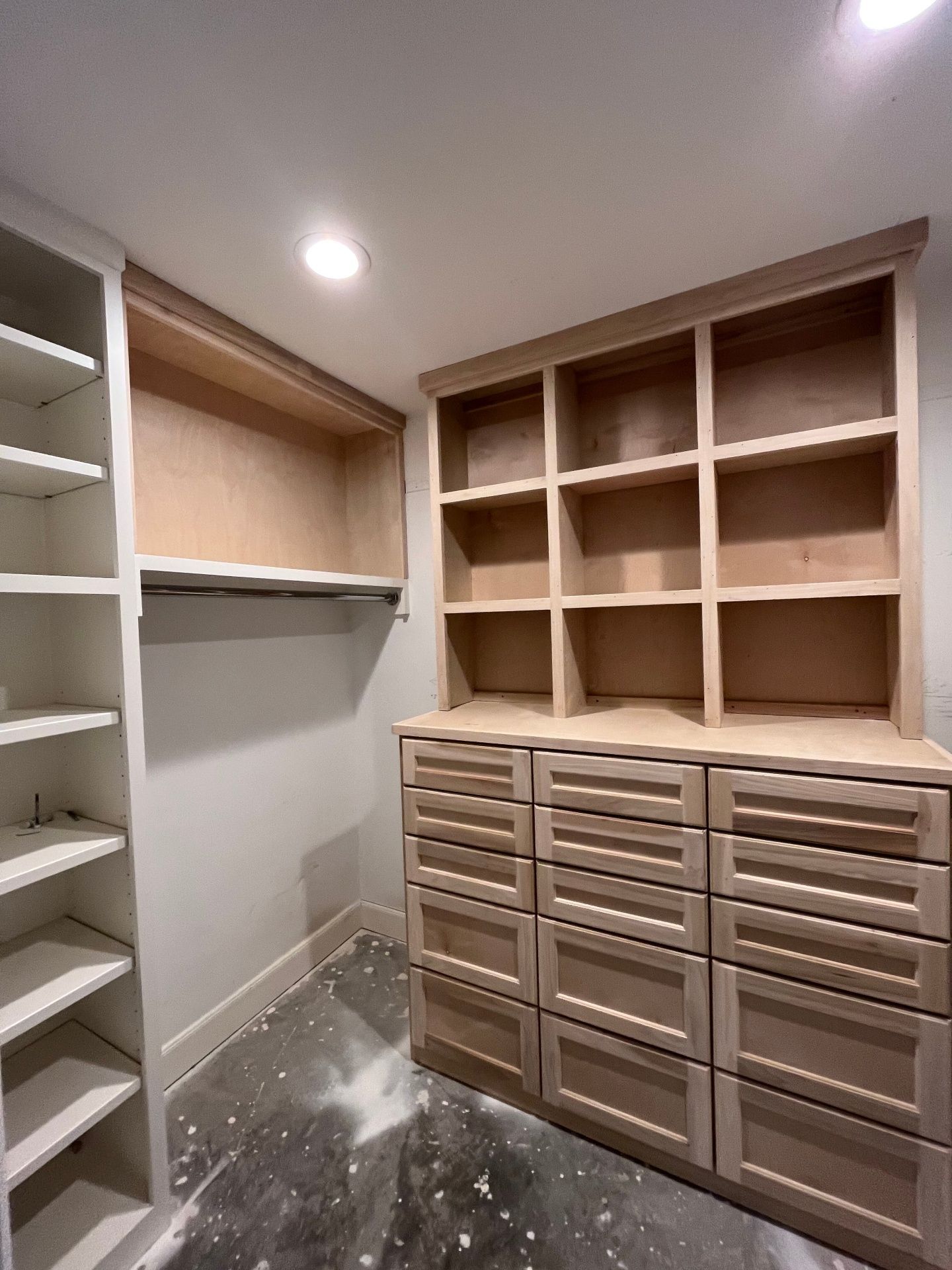 A walk-in closet under construction with unfinished wood shelving and a dresser with drawers, set against a white wall.