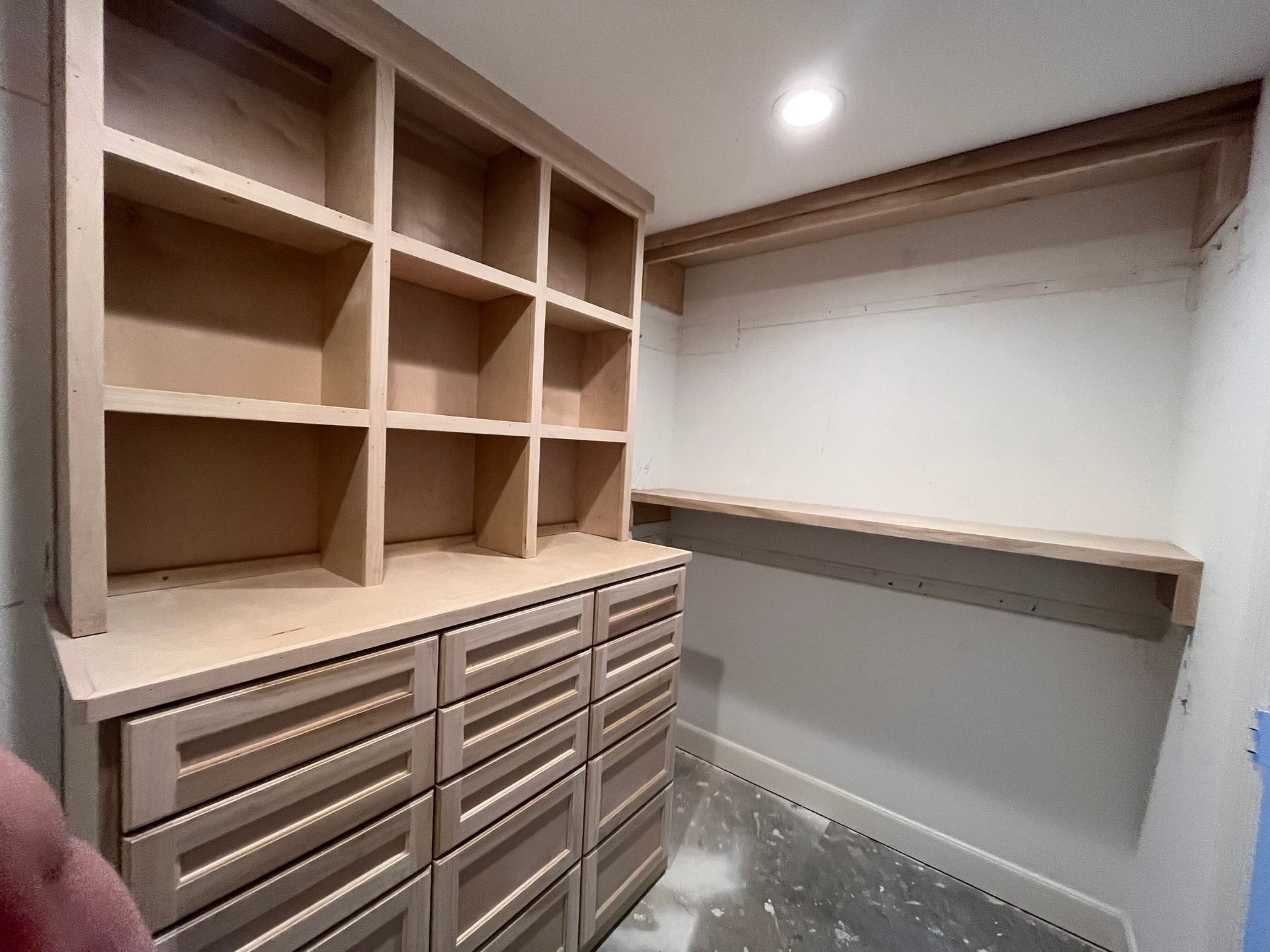 Unfinished light-wood closet shelving unit with drawers and open cubbies installed in a room with white walls.