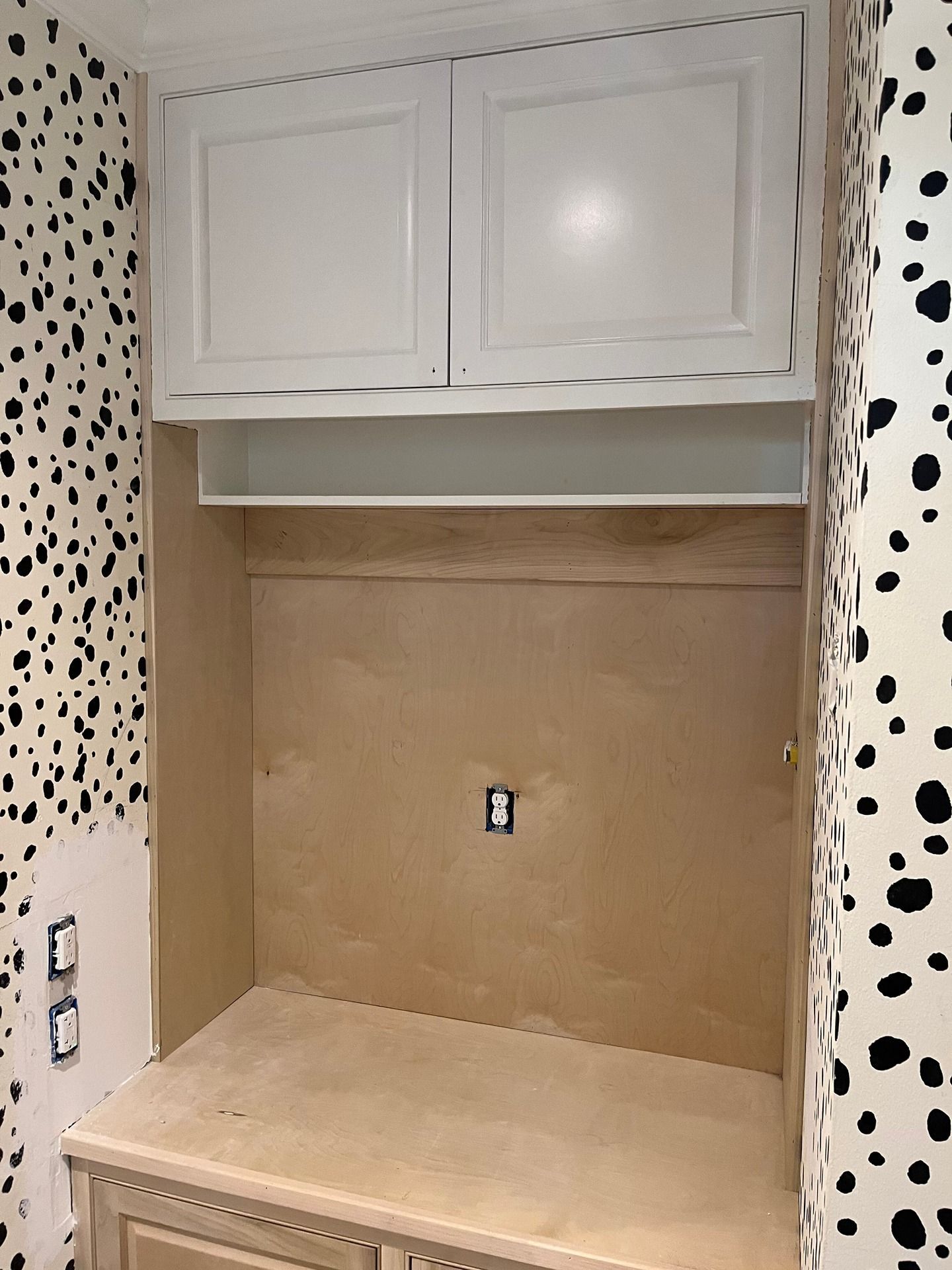 A recessed wall niche featuring upper white cabinets, a central shelf, and an unfinished wooden countertop and backboard.