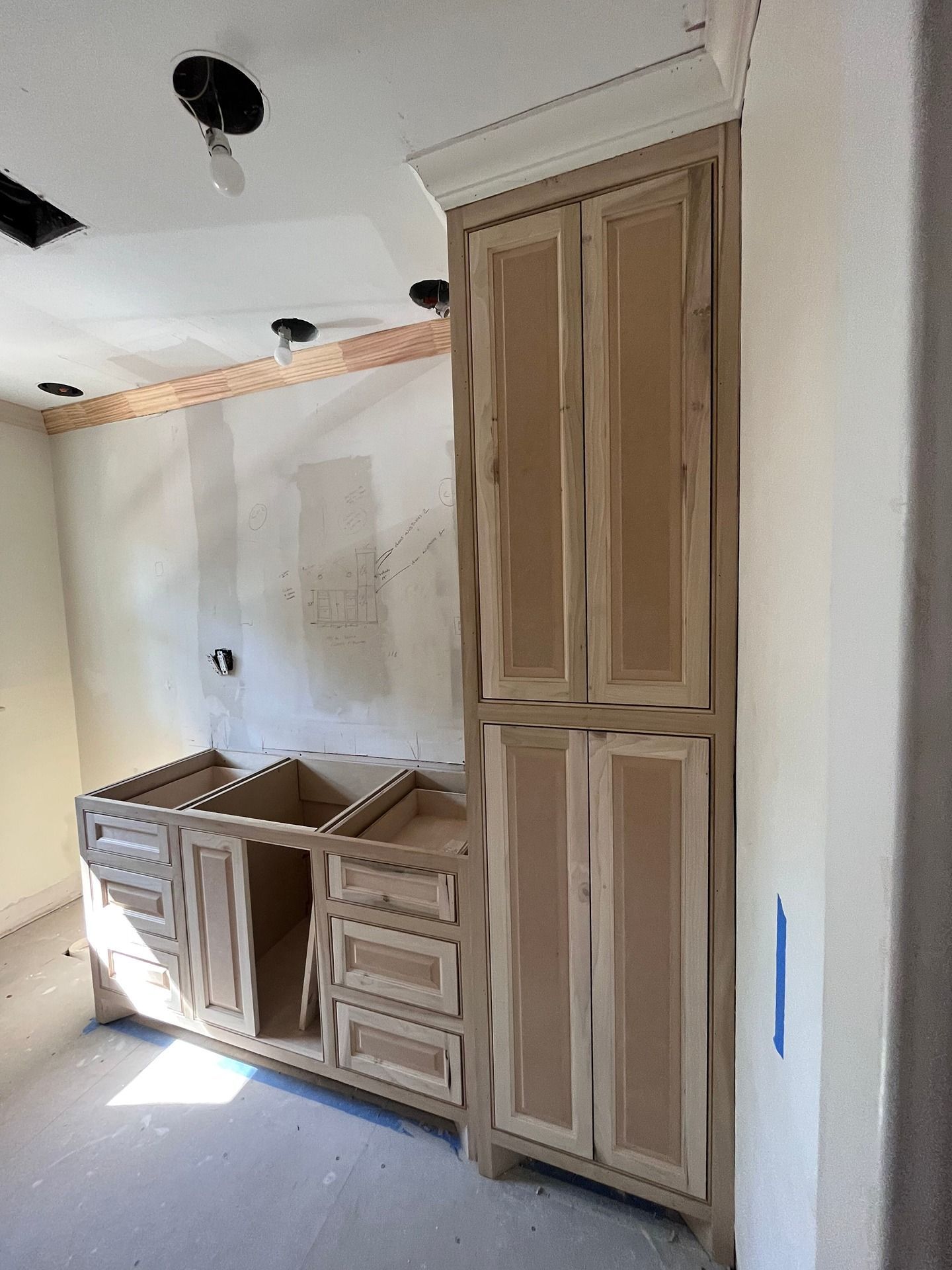 Unfinished wooden bathroom vanity and matching tall linen cabinet installed in a room under renovation.