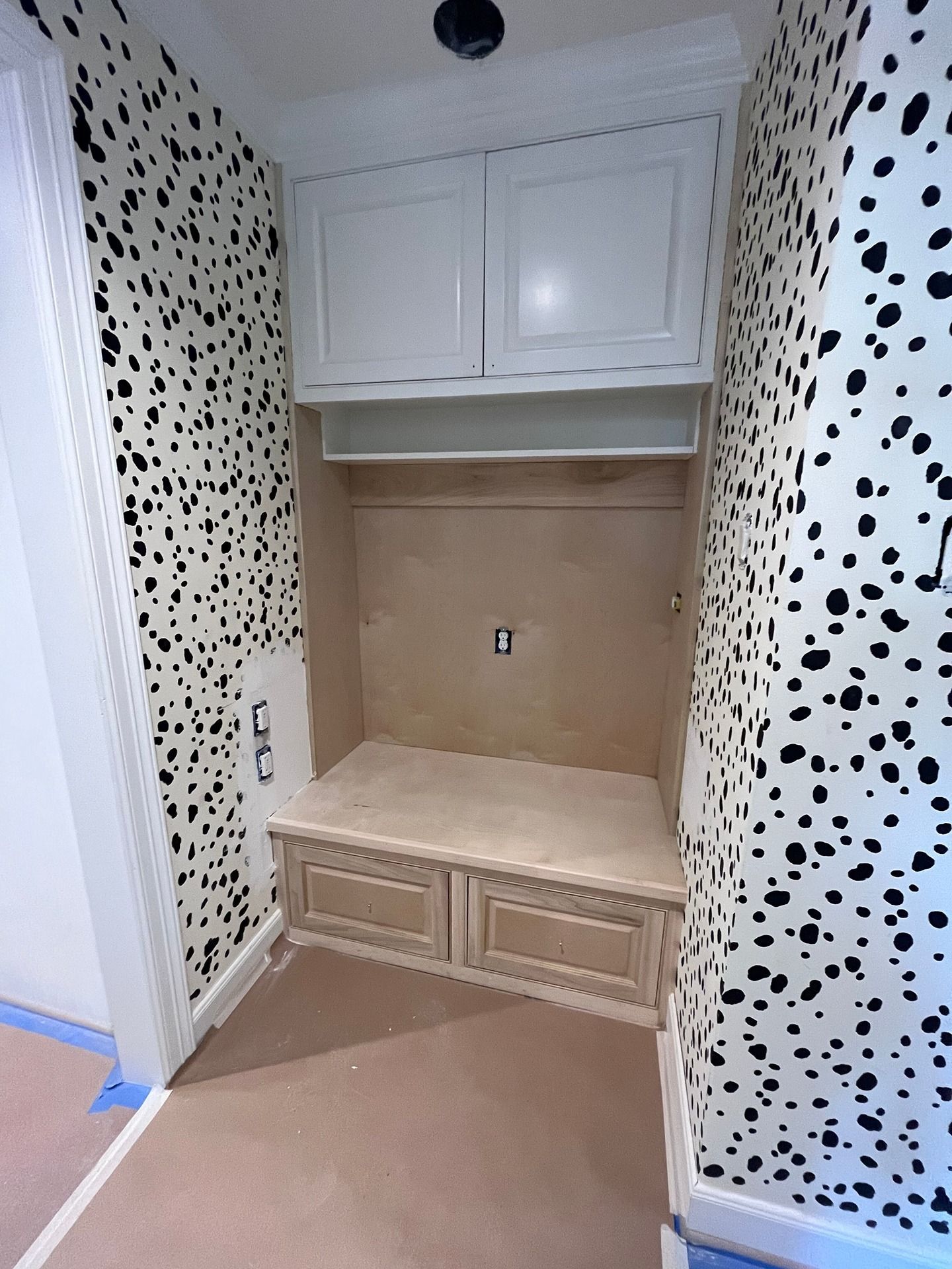 Built-in mudroom bench and upper cabinets set against walls with a black and white dalmatian-print wallpaper.