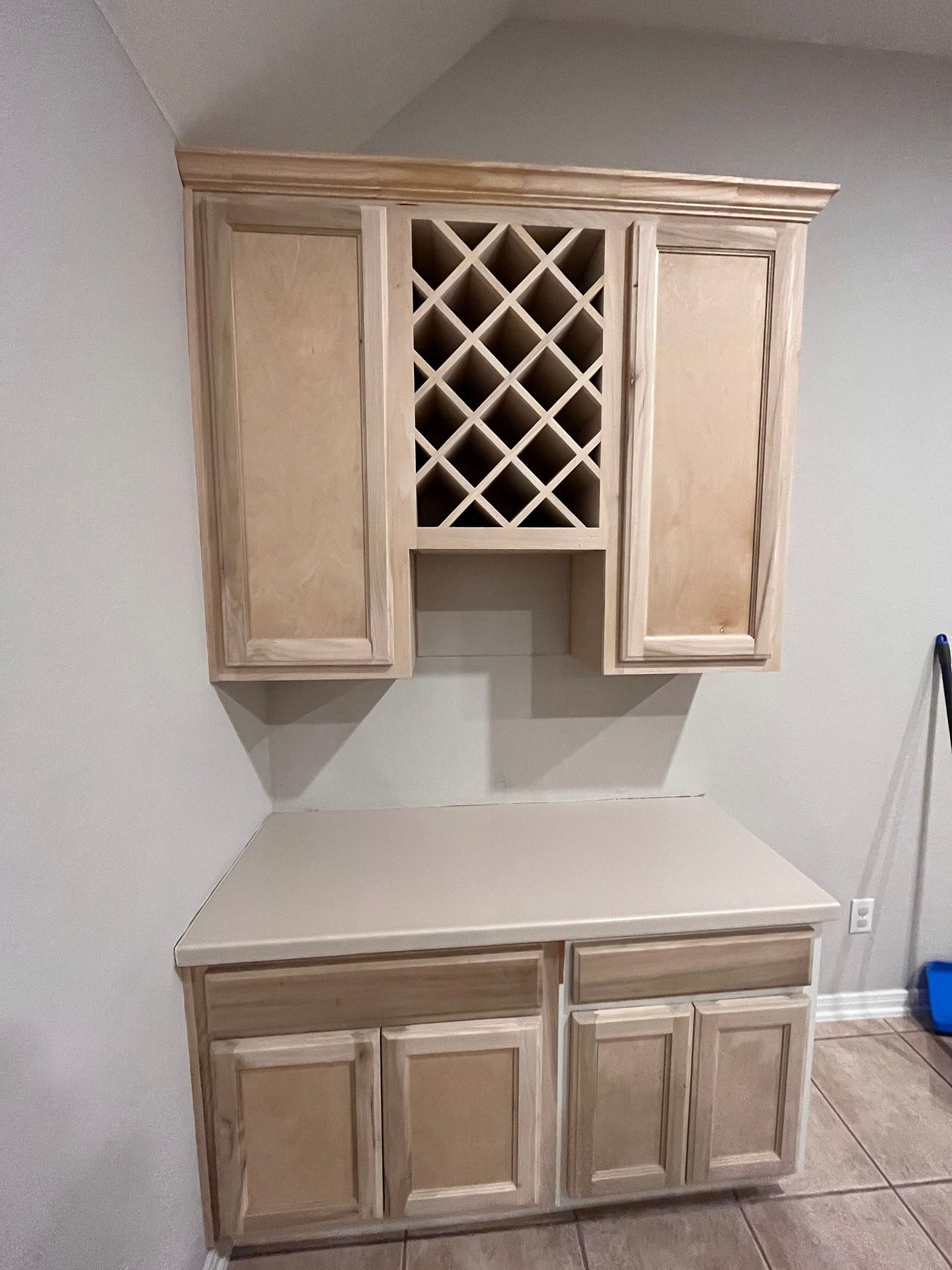 Unfinished light wood cabinetry featuring a wine rack, upper and lower cabinets, and a countertop in a kitchen area.
