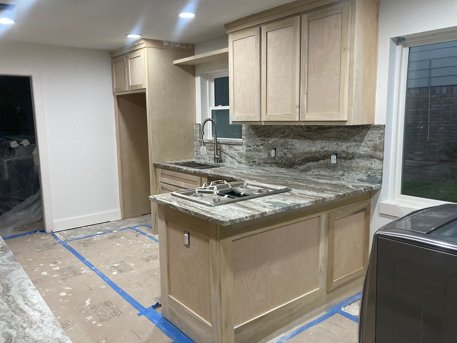 Unfinished kitchen with natural wood cabinets, granite countertops, an undermount sink, and protective floor paper.