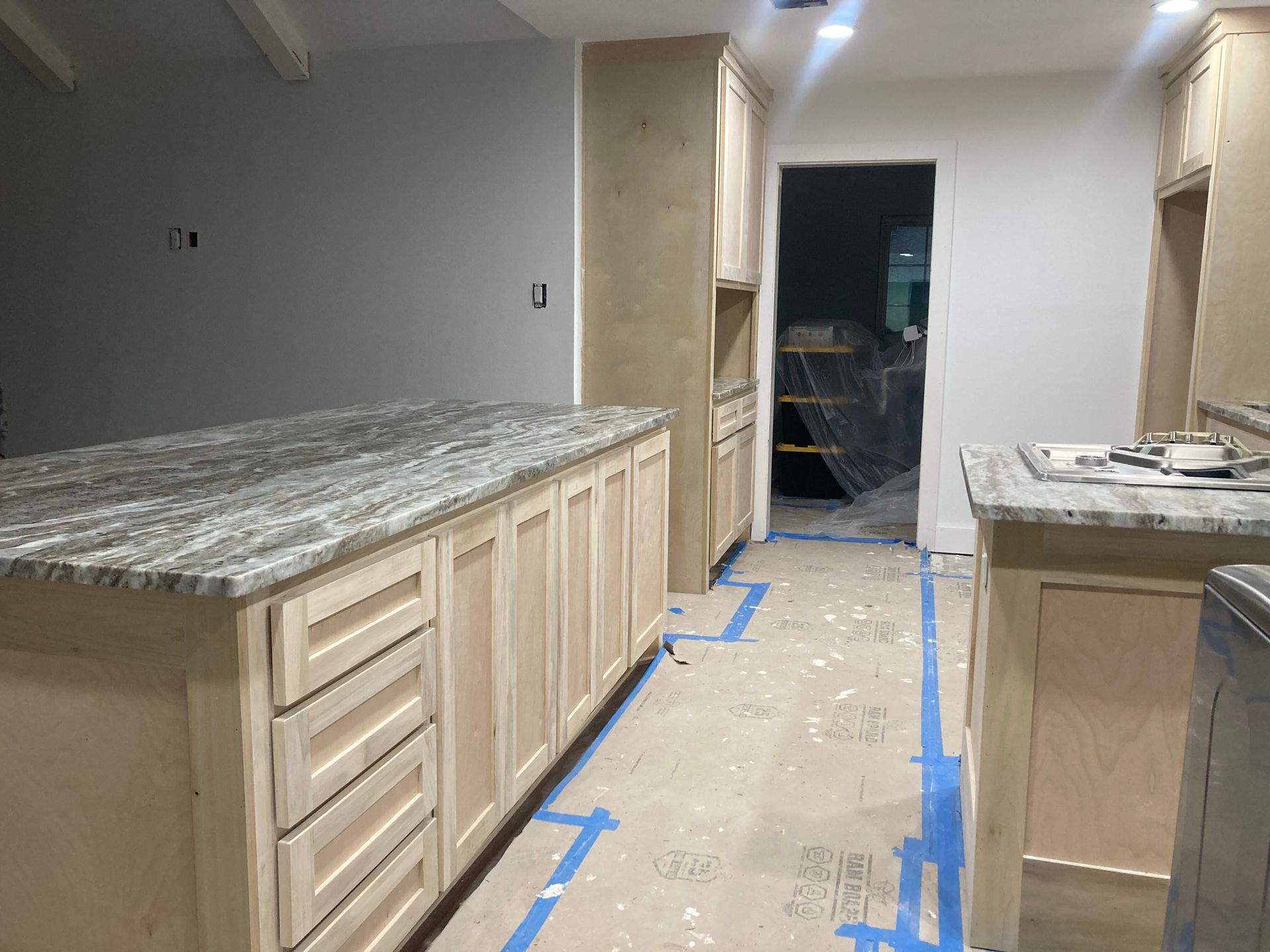 A kitchen under construction with unpainted light wood cabinets and grey, speckled stone countertops.