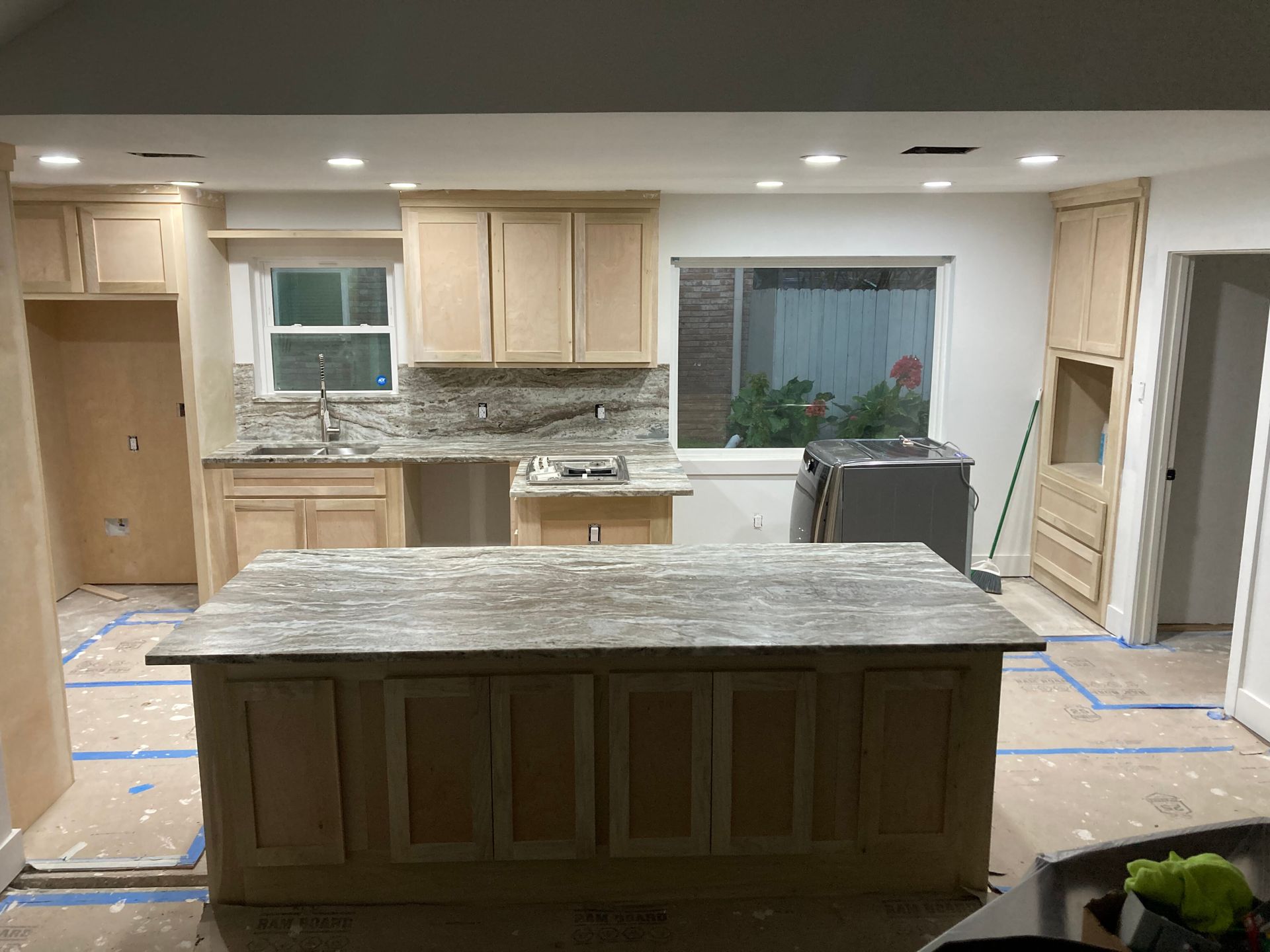 A kitchen under renovation featuring natural wood cabinets, a large central island, and protective floor covering.