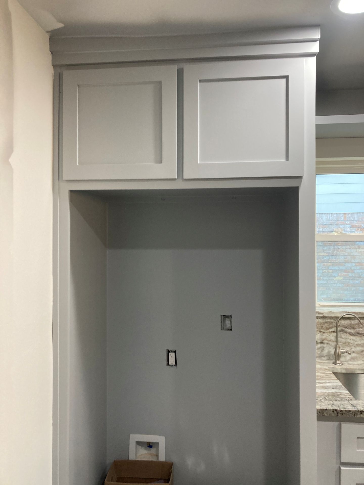 A light gray kitchen cabinet built over a refrigerator alcove with electrical outlets on the back wall.