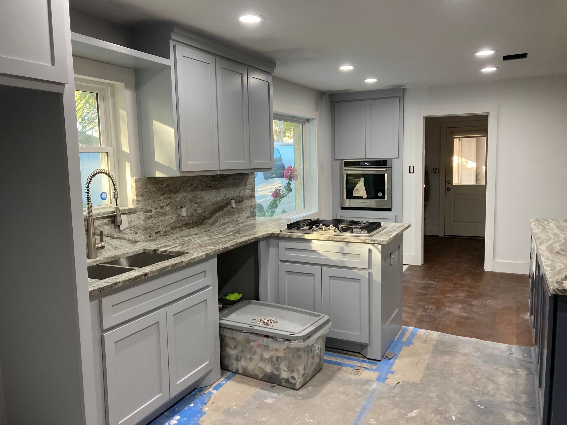 A kitchen undergoing renovation with light gray cabinets, granite countertops, an installed oven, and unfinished flooring.