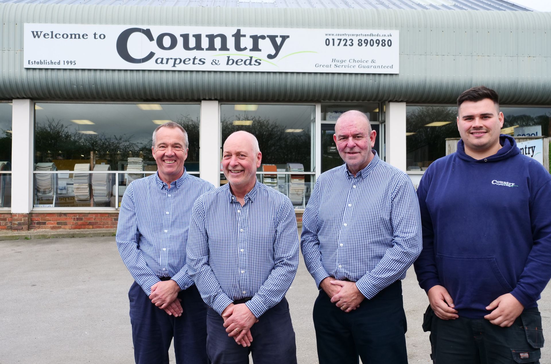 Four men are standing in front of a country carpets and beds store.