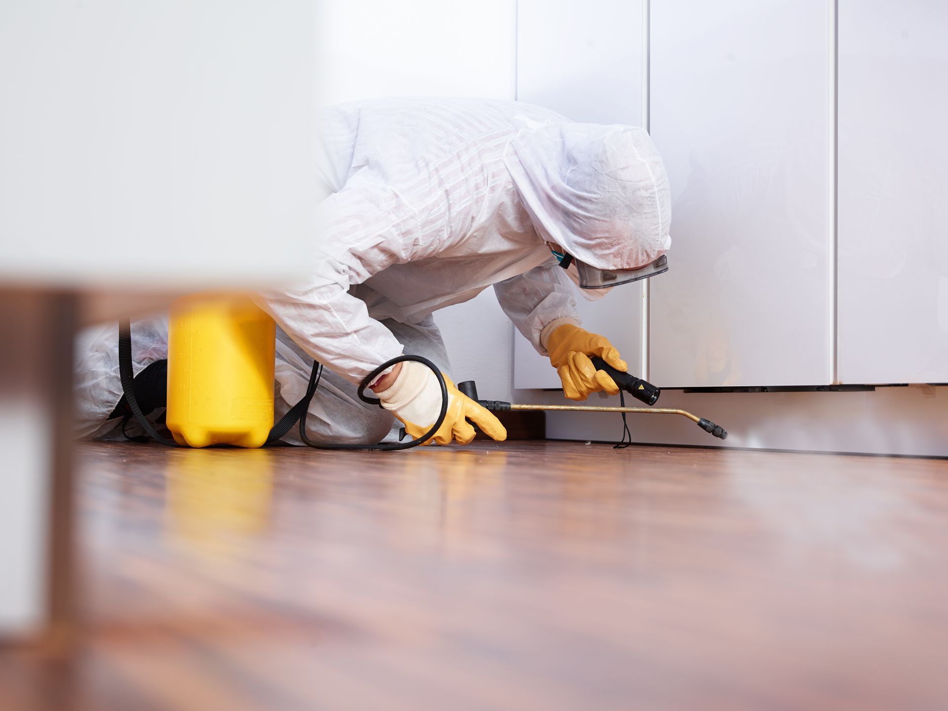 A man in a protective suit is spraying a chemical on a wooden floor.