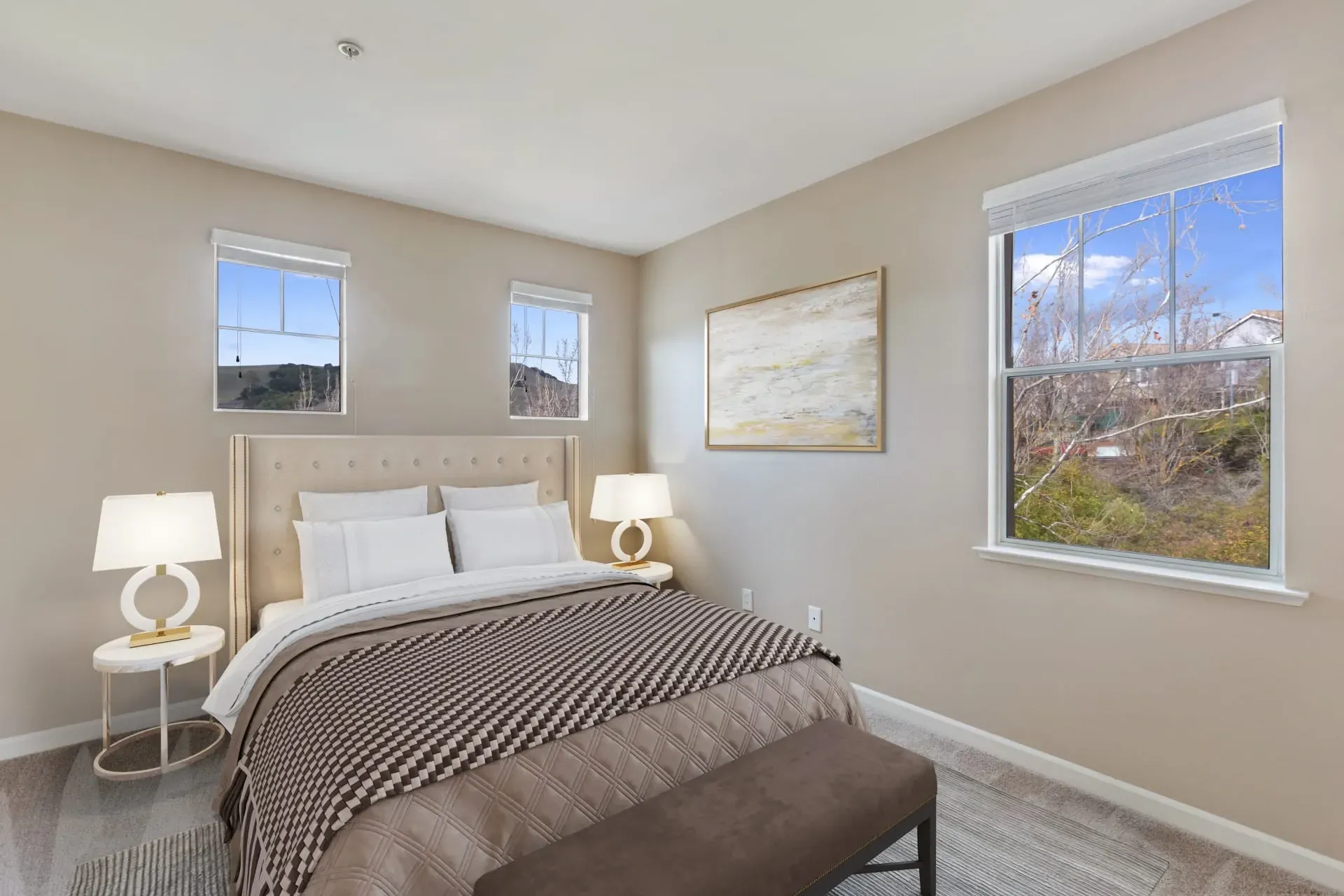 Bedroom with a queen-sized bed, two nightstands with lamps, and a bench at the foot of the bed.