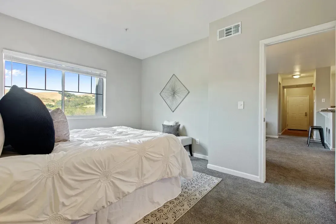 Bedroom with a large window, a king-size bed, and a view of rolling hills.