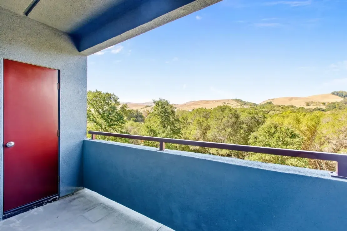 Balcony view with red door and green trees.