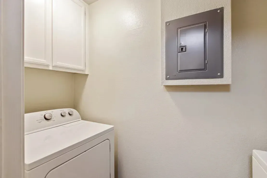 In-unit washer and dryer with white cabinets above and an electrical panel on the wall.