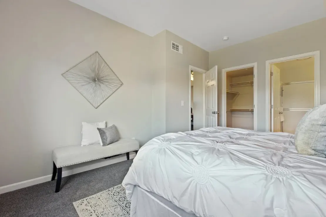 Cozy bedroom featuring a large bed, bench, and a glimpse into a walk-in closet and en-suite bathroom.