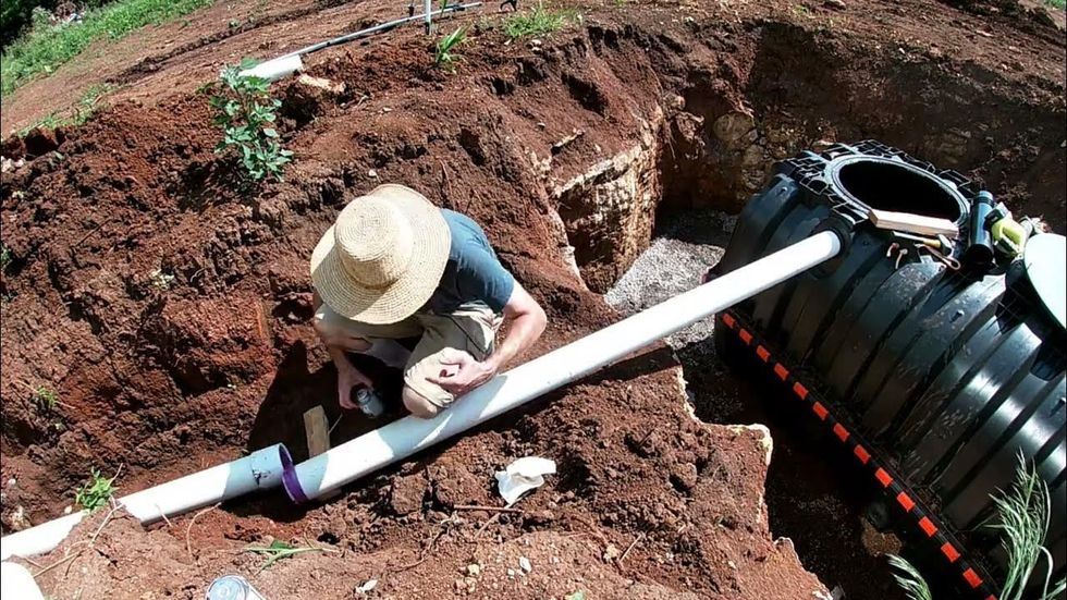 A man in a straw hat is working on a pipe in the dirt