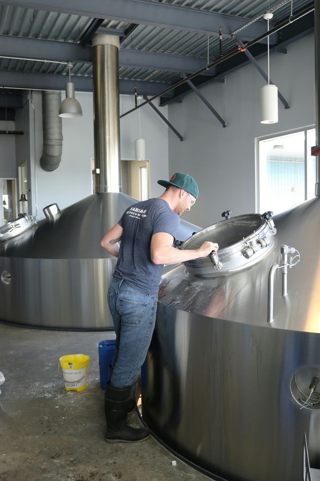 A man is standing next to a large metal tank in a brewery.