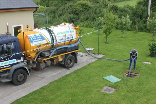 A man is standing next to a vacuum truck in a yard.