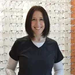 A woman is smiling in front of a wall of glasses.