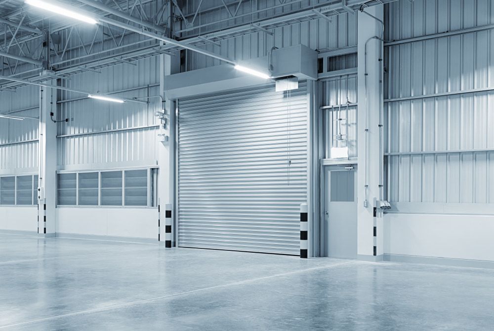 An Empty Warehouse with A Rolling Door and A Concrete Floor — Fraser Coast Waterproofing in Torquay, QLD