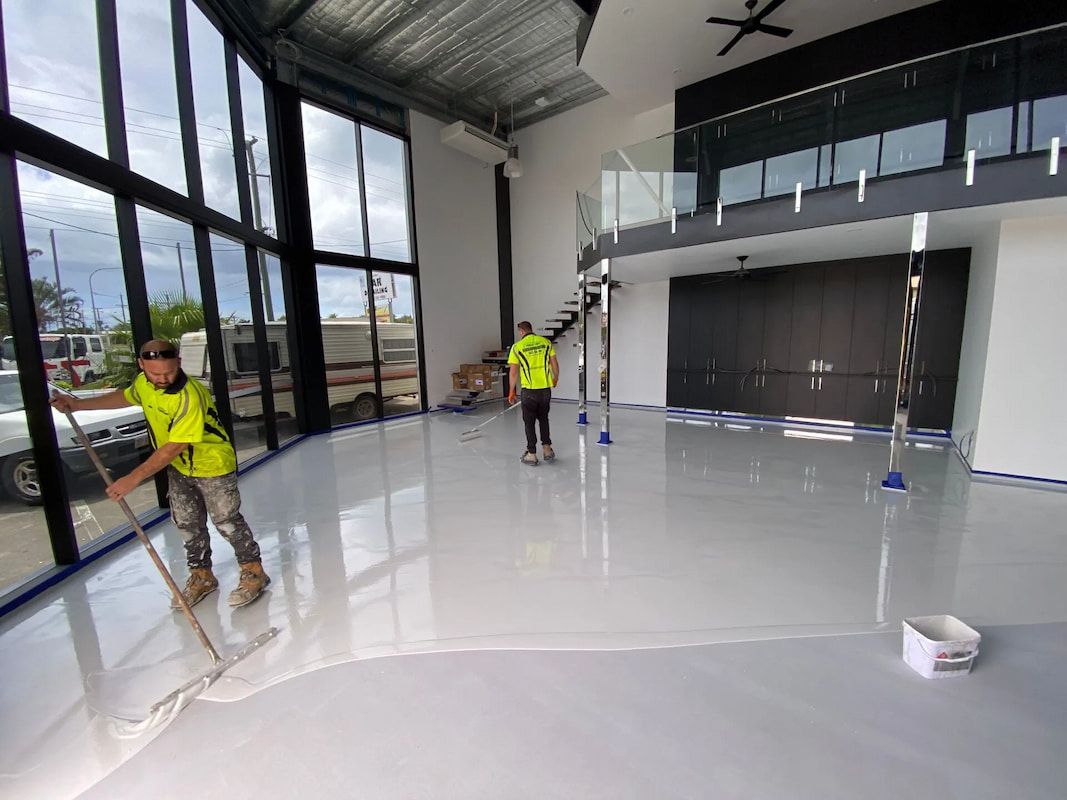 Two Men Are Painting a White Floor in A Large Room — Fraser Coast Waterproofing in Pialba, QLD