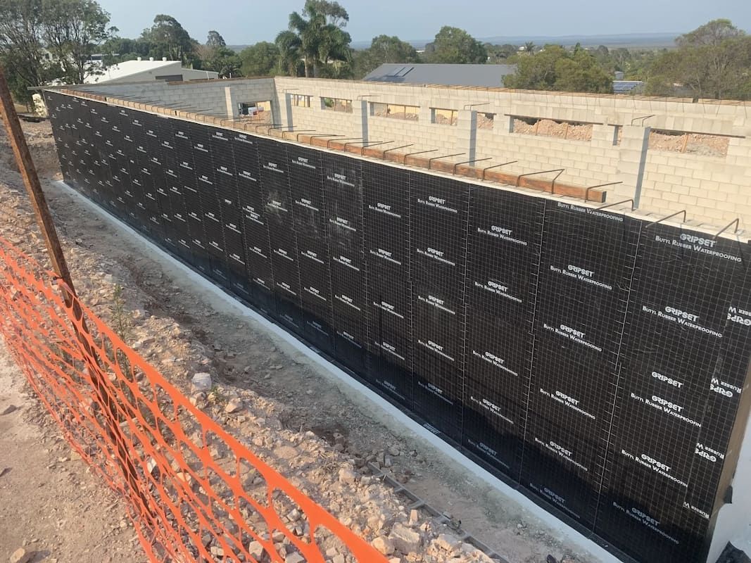 A Large Black Wall Is Surrounded by An Orange Fence — Fraser Coast Waterproofing in Pialba, QLD