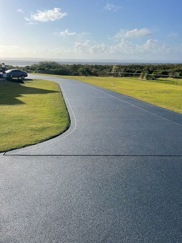 A Driveway Leading to A Grassy Field with A View of The Ocean — Fraser Coast Waterproofing in Pialba, QLD