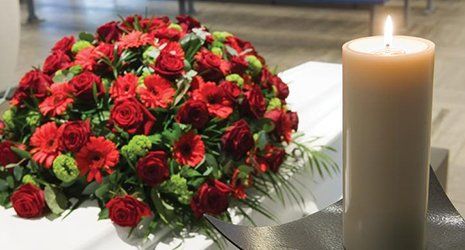 Un bouquet di crisantemi di color rosso su una bara di colore bianco e una candela bianca accesa 