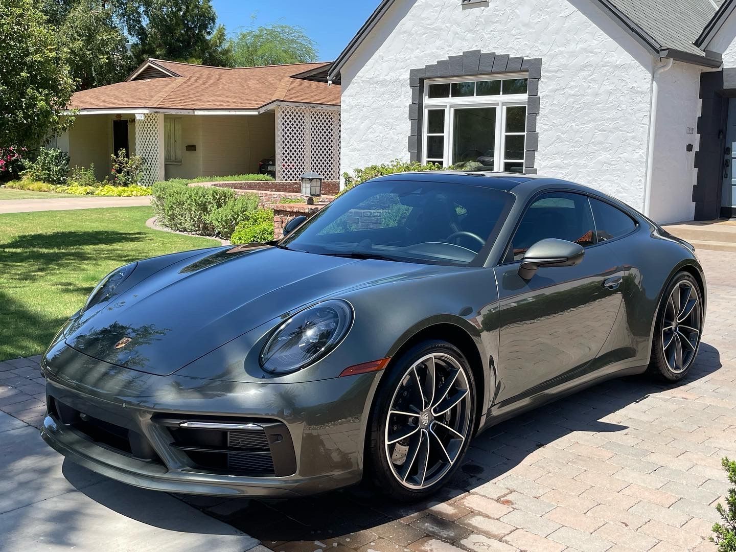 A gray porsche 911 is parked in front of a white house.