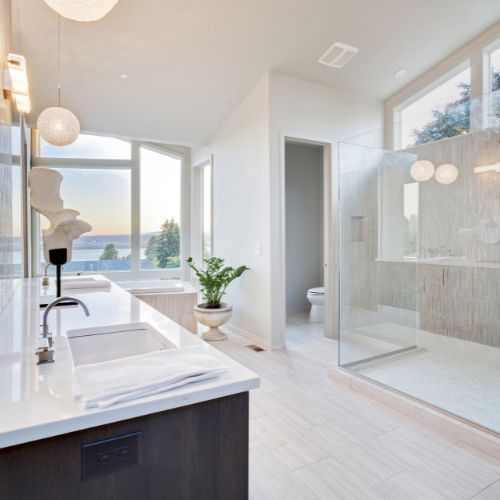 Modern bathroom with white countertops, large windows overlooking water, glass shower. Modern bathroom with white countertops, large windows overlooking water, glass shower.