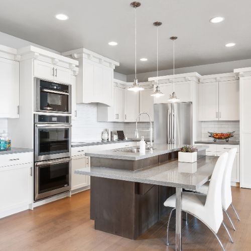 White kitchen with island, stainless steel appliances, and pendant lights. White kitchen with island, stainless steel appliances, and pendant lights.