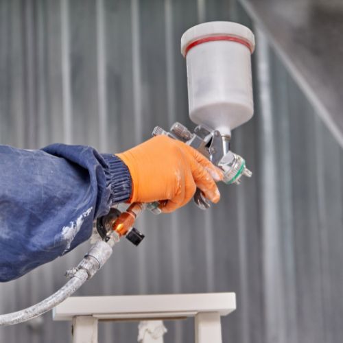 Person wearing orange glove spraying white paint with spray gun. Person wearing orange glove spraying white paint with spray gun.