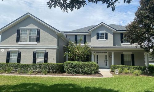 Two-story gray house with black shutters, white door, and green lawn. Two-story gray house with black shutters, white door, and green lawn.