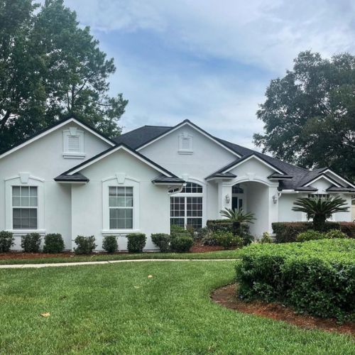 White house with black roof, trimmed with white, lush green lawn, and shrubbery. White house with black roof, trimmed with white, lush green lawn, and shrubbery.
