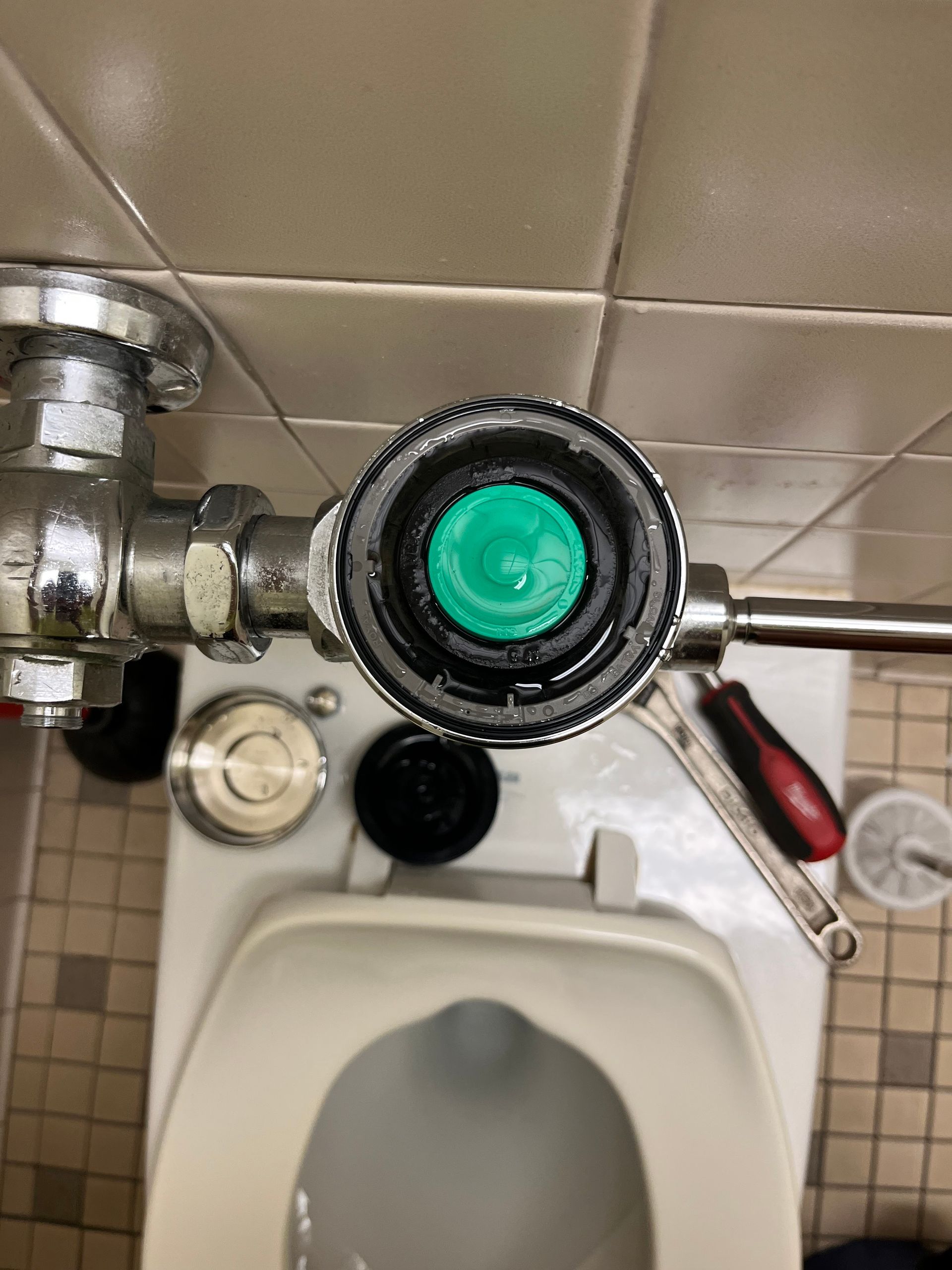 A toilet with a green button on the top of it.