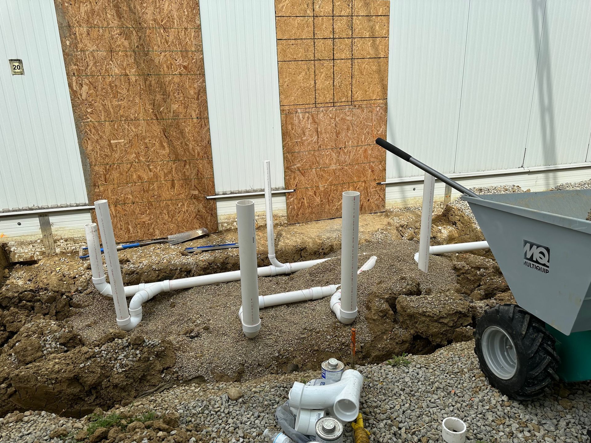 A wheelbarrow is sitting in the dirt next to a pile of pipes.