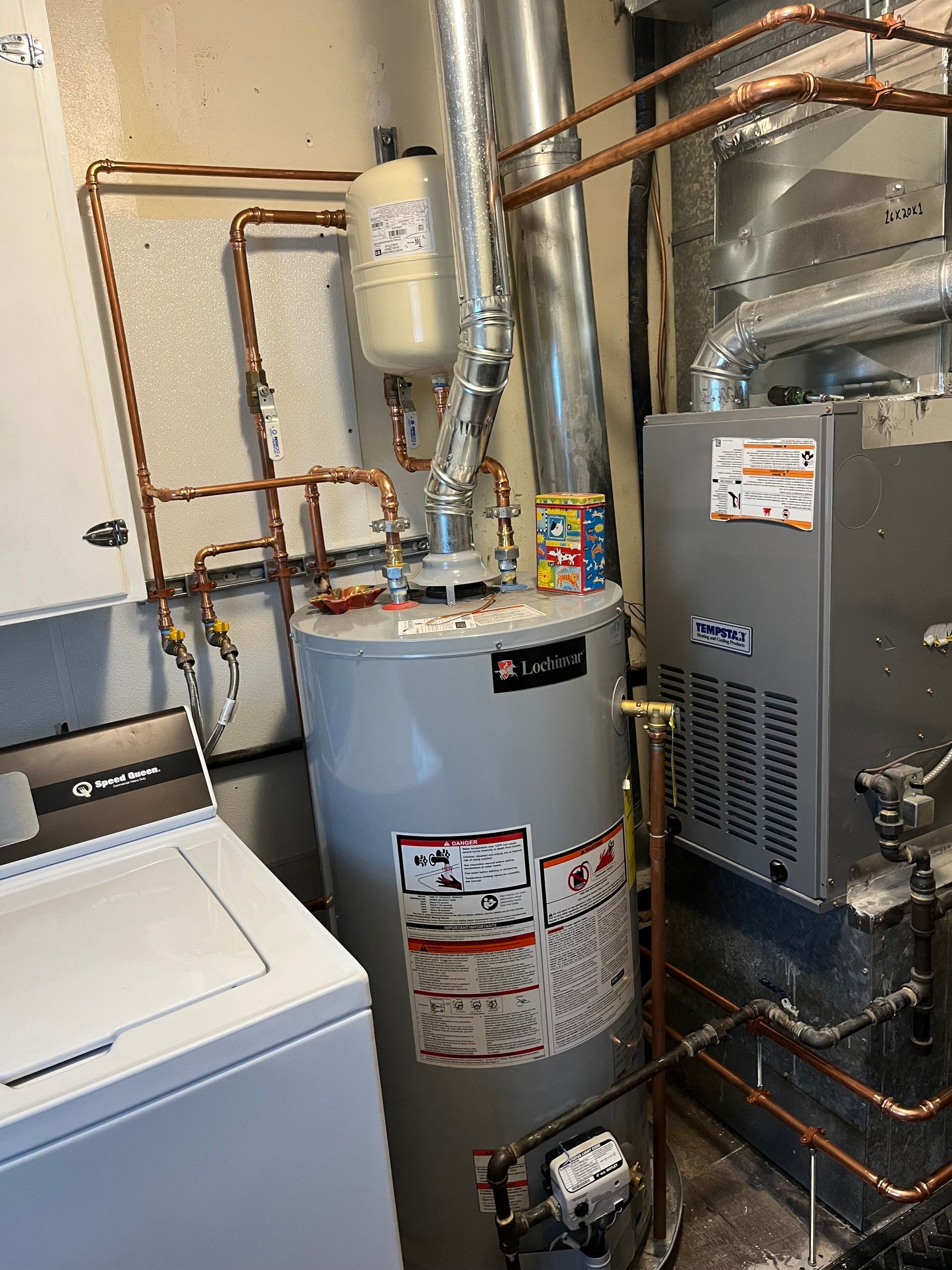 A water heater is sitting next to a washer and dryer in a laundry room.