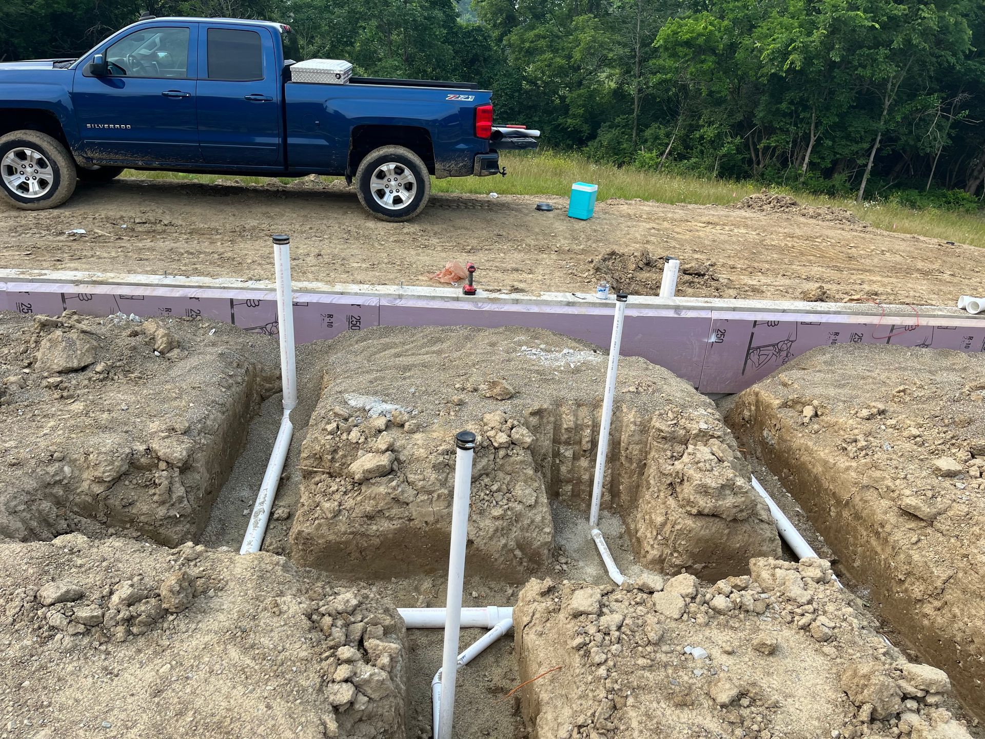 A blue truck is parked in the dirt next to a pile of pipes.