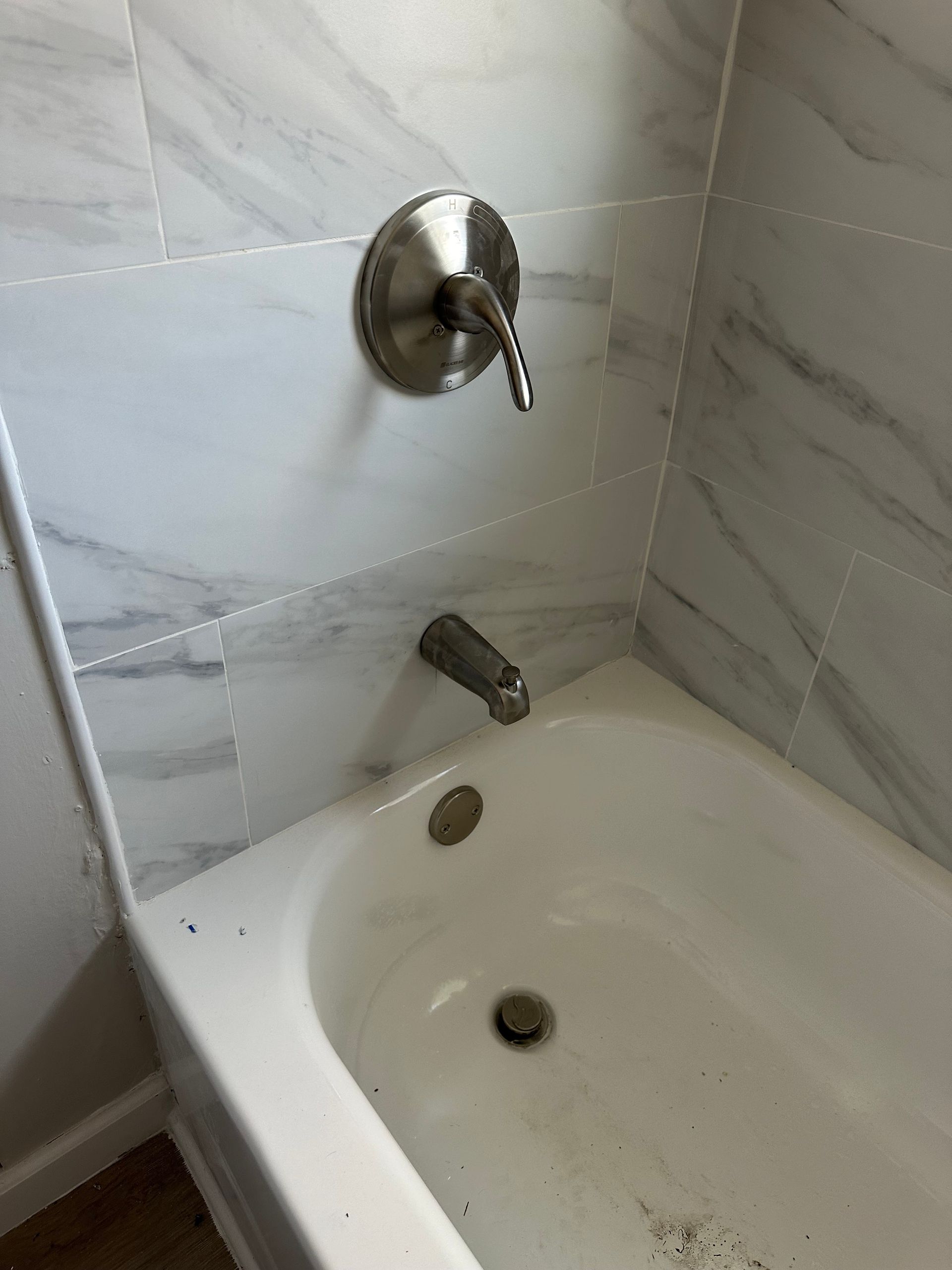 A bathtub in a bathroom with marble tiles and a faucet.