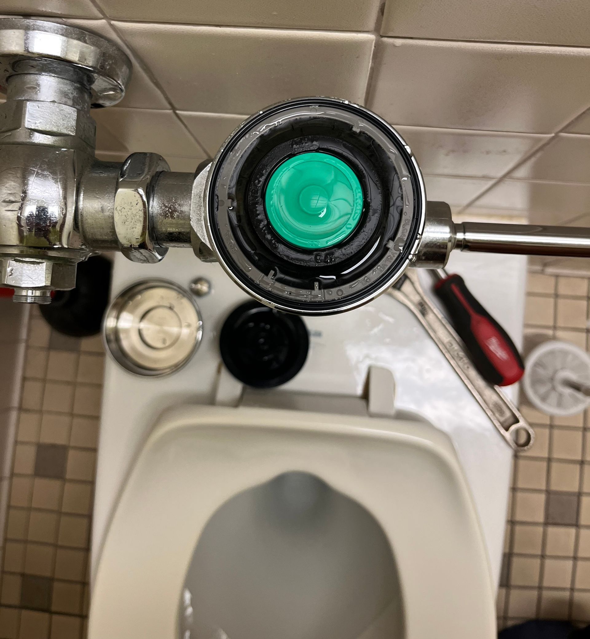 A toilet with a green button on the top of it
