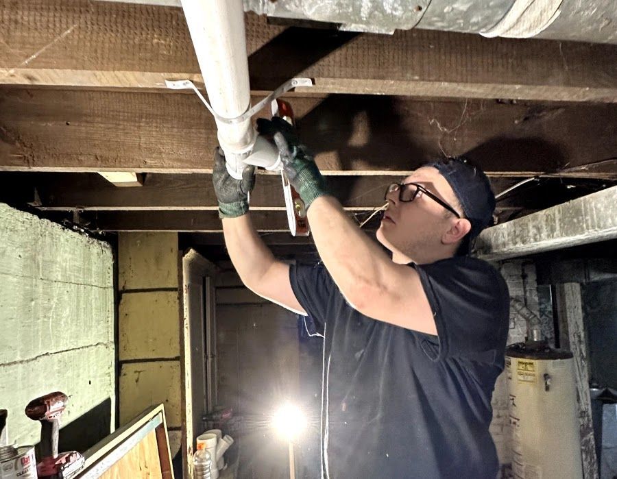 A man is working on a pipe in a basement.